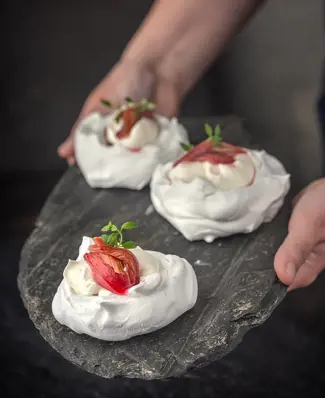 Denne pavlova er lavet på aquafaba-marengs, toppet med græsk yoghurt-skum og sukkersyltede rabarber – en dessert, hvor t...